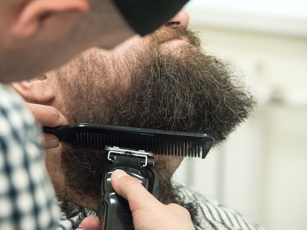 Tailler la barbe avec des tondeuses dans un salon de coiffure. Fermer.