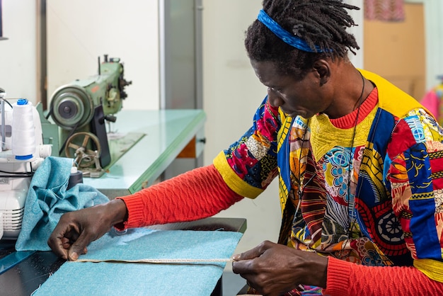 Tailleur africain vêtu de vêtements et de tissus traditionnels au travail dans son atelier de production de vêtements uniques au style moderne et aux couleurs de l'afrique petite entreprise concept d'artisan