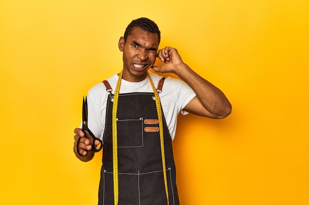 Photo un tailleur afro-américain avec des outils, un studio jaune couvrant les oreilles avec ses mains.