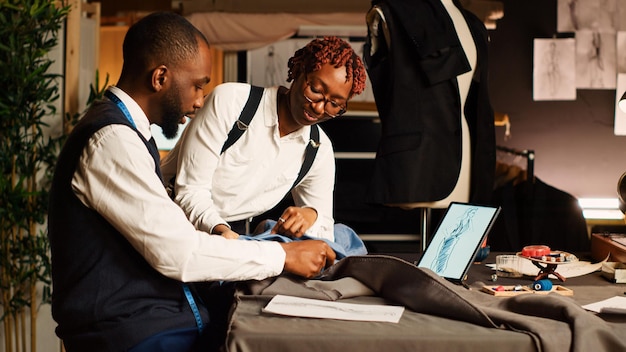 Tailleur et assistant dans la sélection de tissus pour créer des vêtements modernes, travaillant en atelier pour fabriquer des vêtements pour la collection de mode. Deux créateurs choisissant une matière, faite à la main. Tir à la main.