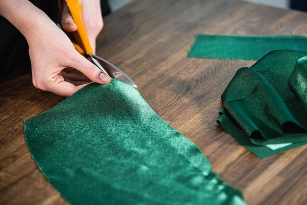 Le tailleur coupe le tissu vert sur la table avec des ciseaux.