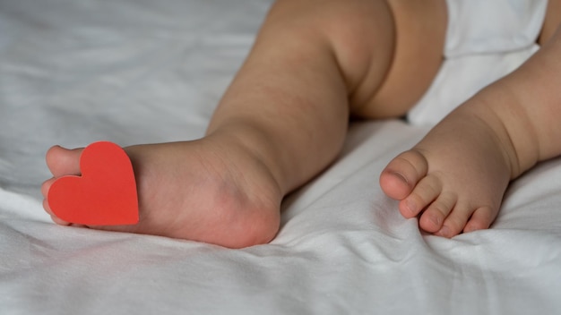 Talons pour enfants bébé allongé sur le lit sous la couverture avec une étiquette sur le doigt avec un coeur Saint Valentin