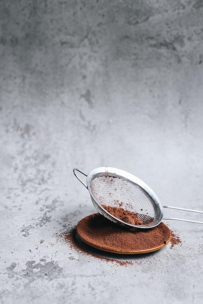 Tamiser la poudre de cacao à l'aide d'une passoire et d'un plateau en bois sur fond gris