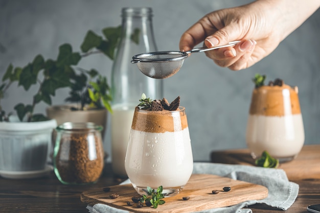 Tamiser la poudre de cacao au tamis sur un verre de boisson mousseuse glacée Dalgona Coffee