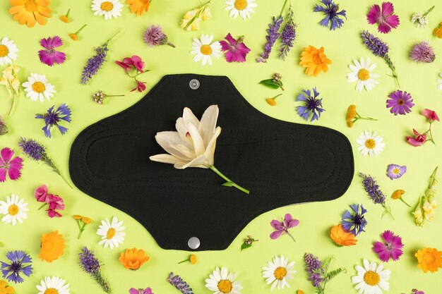 Tampon menstruel réutilisable noir sur une surface verte avec des fleurs sauvages naturelles