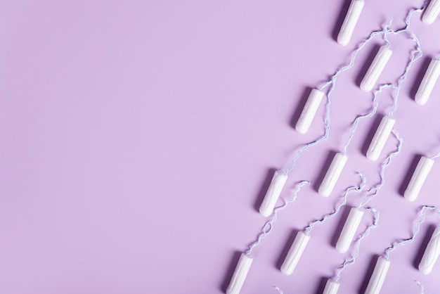 Les tampons pour femmes se trouvent beaucoup dans une ligne sur un fond lilas pastel à plat