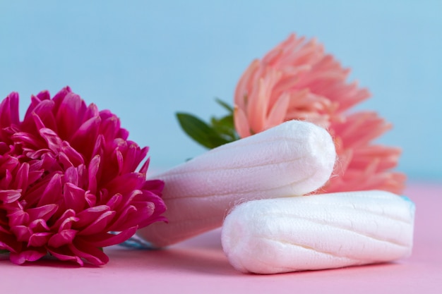 Tampons pour les jours critiques et des fleurs sur une table rose. Soins d'hygiène pendant la menstruation. Cycle menstruel. Prendre soin de la santé des femmes. Protection mensuelle