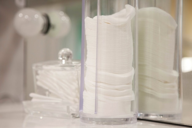 Photo tampons ronds en coton blanc et bâtonnets d'oreille en coton dans des récipients spéciaux pour le stockage et l'utilisation. produits d'hygiène, cosmétiques pour les soins de la peau à l'intérieur du salon de beauté. concept de mode de vie sain. espace de copie