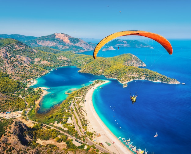 Tandem de parapente survolant la mer avec de l'eau bleue et des montagnes en journée ensoleillée