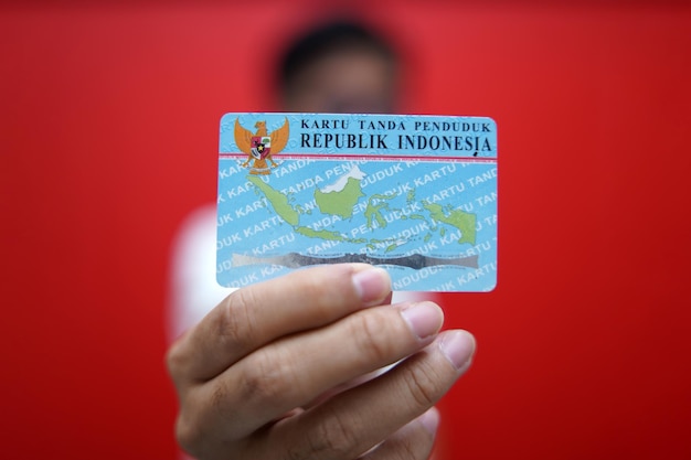 Photo tangerang indonésie 03 avril 2023 une personne montrant et détenant une carte d'identité indonésienne ktp utilisant un t-shirt rouge et un fond rouge mise au point sélective