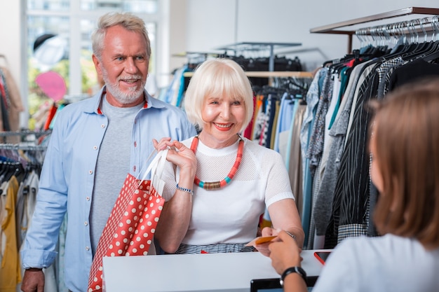 Étape d'achat finale. Famille âgée positive passant une carte de crédit à la vendeuse tout en étant satisfaite de leurs achats en magasin