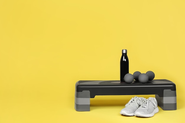 Étape plate-forme haltères bouteille d'eau et baskets sur fond jaune espace pour le texte Équipement de sport
