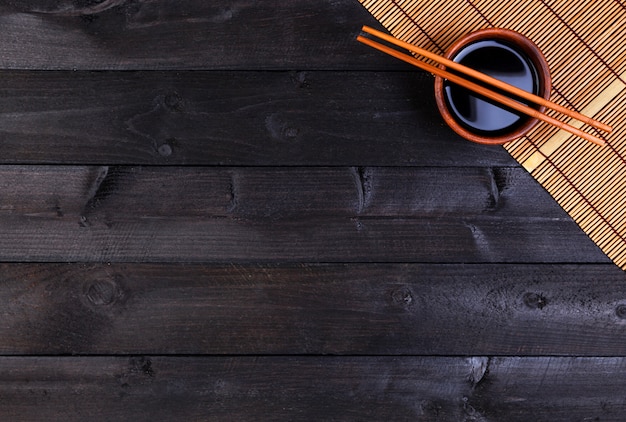 Tapis de bambou, sauce soja, baguettes sur table sombre