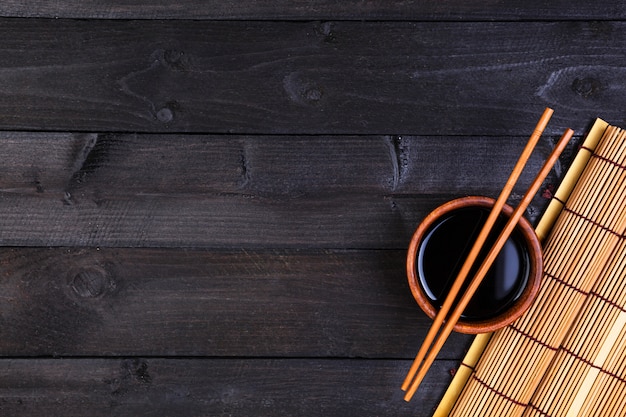 Tapis de bambou et sauce soja sur table en bois foncé. Vue de dessus