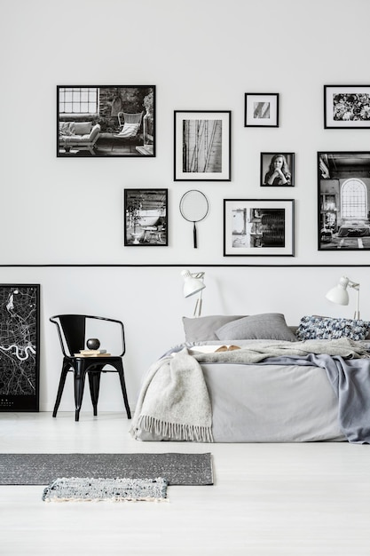 Tapis et chaise noire à côté du lit à l'intérieur de la chambre blanche avec galerie d'affiches Photo réelle