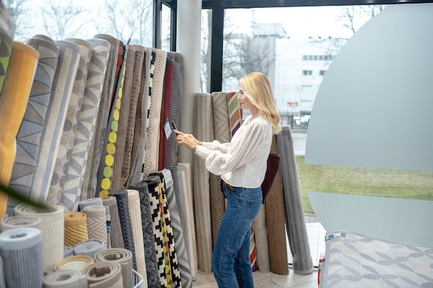 Tapis, un choix. Femme aux cheveux jusqu'aux épaules avec un smartphone debout devant les tapis et prendre une photo dans le salon de meubles.