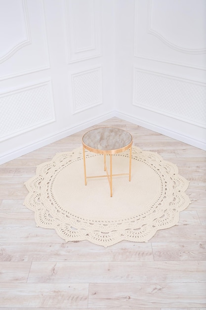 Un tapis en coton tricoté et une table ronde décorative se trouvent sur le sol dans le contexte de l'intérieur Tapis fait main Beige Handwork