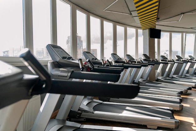 Tapis de course vides dans le club de remise en forme. Beaucoup de machines en marche près de la fenêtre panoramique dans la salle de sport.