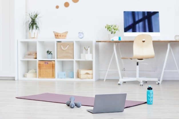 Tapis d'exercice avec haltères et ordinateur portable sur le sol préparé pour l'entraînement sportif à la maison