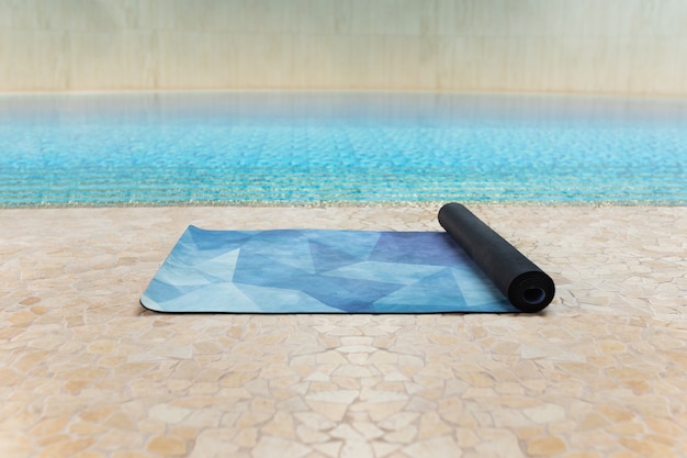 Tapis de yoga bleu à l'intérieur de la salle de sport après un cours de yoga à l'étage près d'une piscine, gros plan