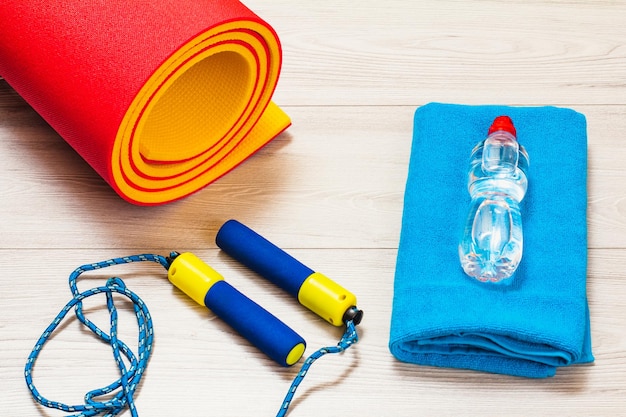 Tapis de yoga et corde à sauter pour le fitness, une serviette, une bouteille d'eau dans une chambre ou une salle de sport sur le sol gris.