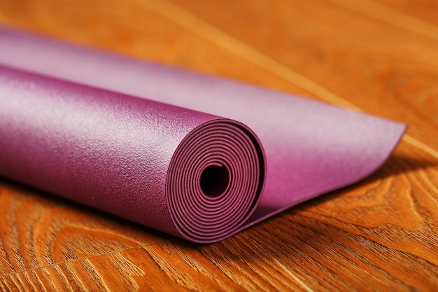 Un tapis de yoga couleur lilas est étalé en rouleau sur le parquet. Fermer