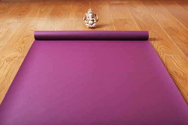 Un tapis de yoga de couleur lilas est étalé sur le sol en bois avec une figurine Ganapati