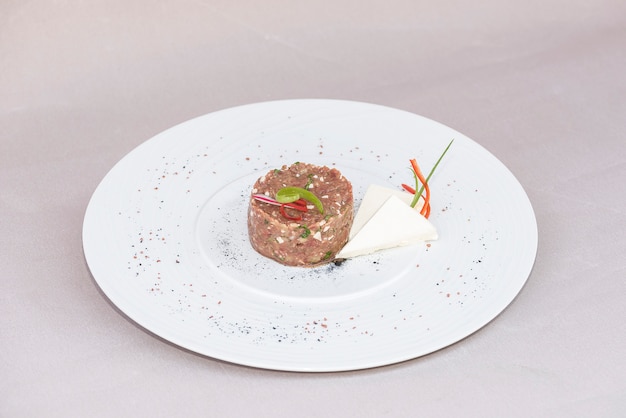 Tartare de boeuf classique, servi avec des tranches de fromage et décoré avec des herbes