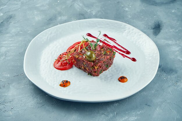 Tartare de boeuf frais aux câpres, épices, oignons sur une assiette blanche. Fermer.