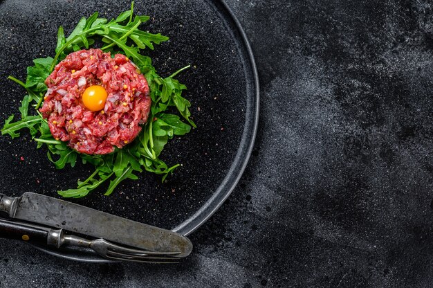 Tartare De Boeuf Avec Un Oeuf De Caille Servi Sur Une Assiette En Pierre Noire.. Fond Noir. Vue De Dessus. Espace De Copie.