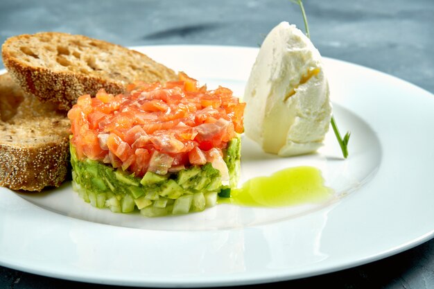 Tartare de saumon et d'avocat, croûtons dans une assiette blanche sur béton