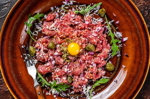 Tartare de steak de boeuf au jaune d'oeuf cru, câpres marinées et parmesan. Fond sombre. Vue de dessus.