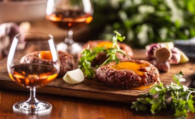 Tartare de steak de bœuf salé servi avec du jaune d'œuf, de l'ail et des herbes sur un bureau en bois. Whisky comme boisson.