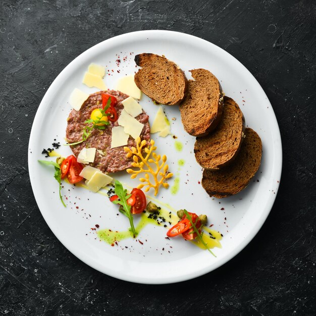 Tartare de veau avec pain grillé et légumes sur une assiette blanche Vue de dessus Style rustique