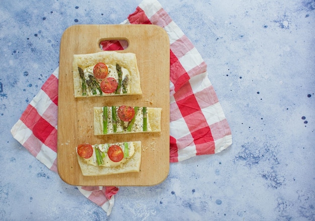 Tarte au fromage à la crème d'asperges vertes et tomates sur une planche à découper en bois sur fond bleu clair