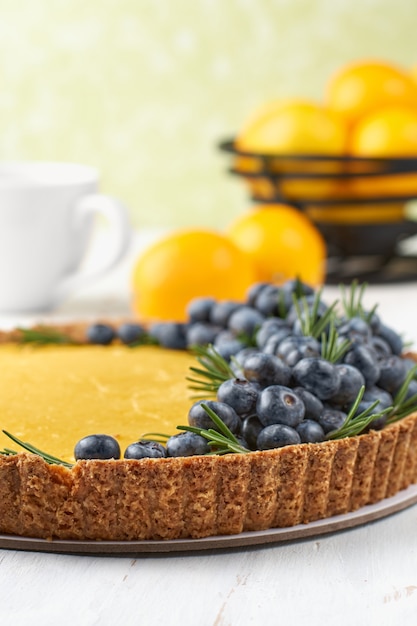 tarte au lait caillé de citron et myrtille fraîche sur une surface en bois clair.