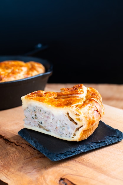 Tarte au porc ou à la viande fait maison concept sur plaque de pierre et poêle en fonte sur fond en bois