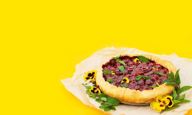 Tarte aux cerises de printemps, décorée de fleurs comestibles sur fond jaune.