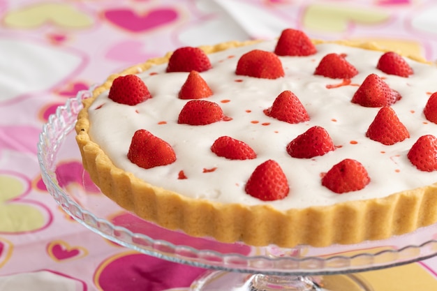 Photo tarte aux fraises à la crème blanche sur une nappe rose romantique décorée de coeurs pour la saint-valentin.