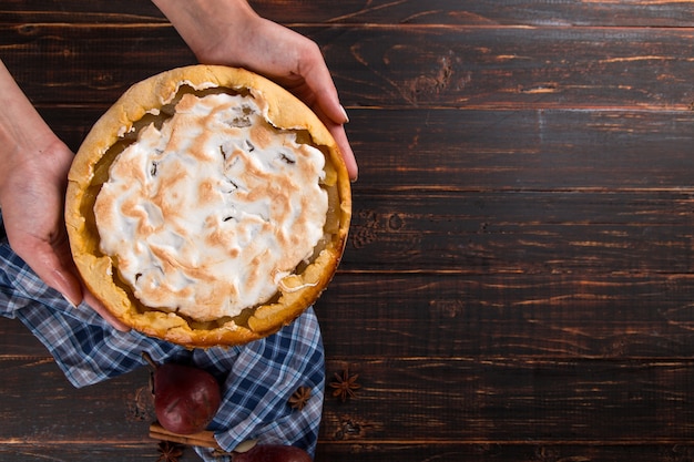 Tarte aux poires à la crème dans les mains des femmes, pâtisseries maison sur table en bois, aux épices. Copiez l'espace.