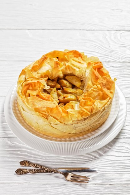 Tarte aux pommes en couches avec croûte phyllo sur un plateau blanc sur une table en bois blanc, vue verticale d'en haut