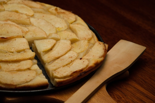 Tarte aux pommes maison et morceau de tarte avec des tranches de pomme à la table de cuisson.