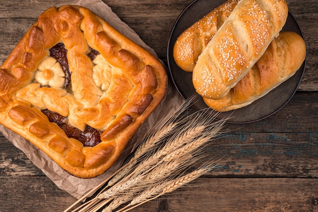 Tarte aux pommes, petits pains frais et épillets de blé sur un fond en bois brun.