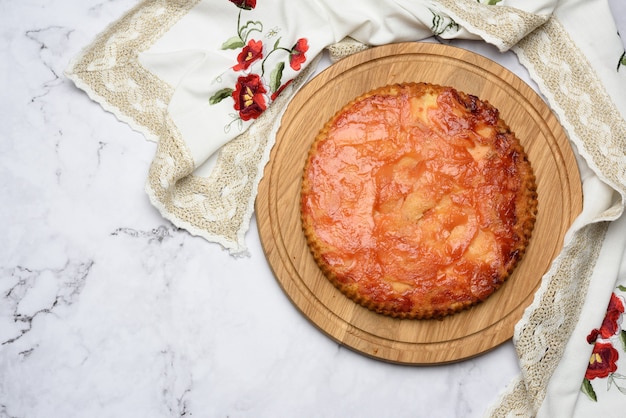 Tarte aux pommes ronde au four sur planche de bois, vue du dessus, table blanche