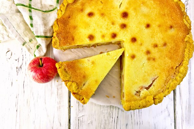 Tarte aux pommes avec sauce à la crème sure sur un parchemin, des fruits et une serviette sur un fond de planche de bois