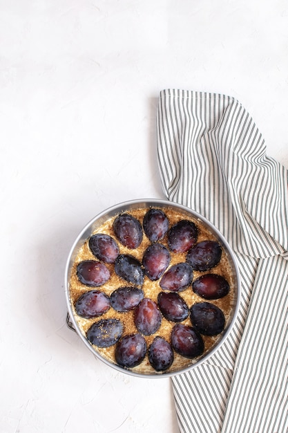 Tarte aux prunes non cuite dans un moule en métal sur une serviette à rayures froissée.