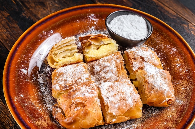 Tarte Bougatsa grecque en tranches avec pâte phyllo et crème pâtissière à la semoule. Fond en bois sombre. Vue de dessus.