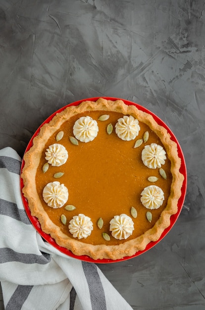 Tarte à la citrouille festive traditionnelle avec des épices, de la crème fouettée et des graines sur une pierre sombre