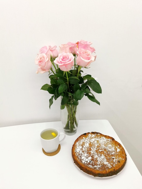 Tarte à la citrouille maison avec un bouquet de roses et de tasses de thé sur un tableau blanc contre