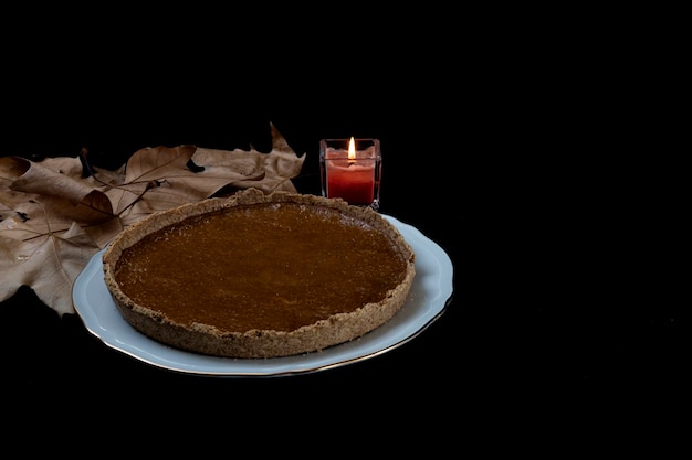 Tarte à la citrouille maison sur fond noir avec feuille d'automne et bougie